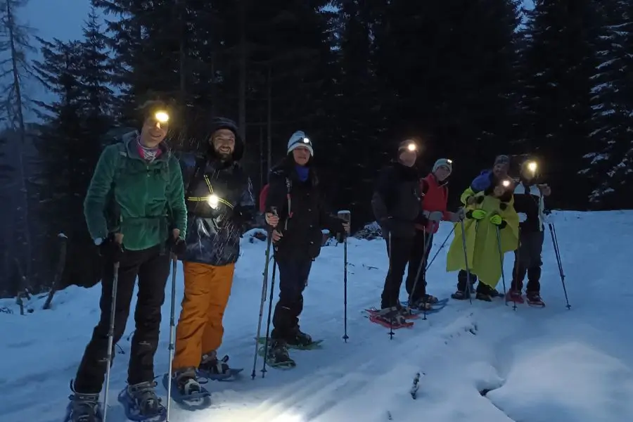 A group of hikers with headlamps during a night snowshoe hike through the snowy forests of the Dolomites with WeHike.