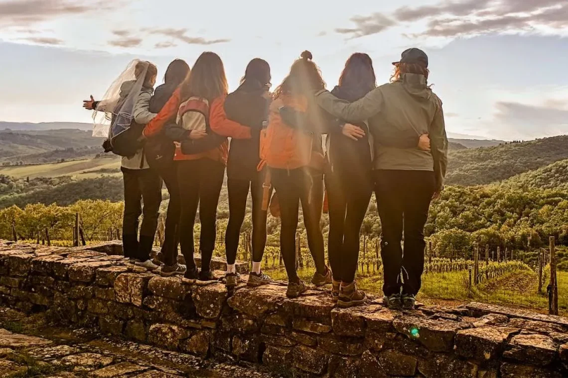 Amiche abbracciate guardano il tramonto sulle colline del Chianti durante l’addio al nubilato.